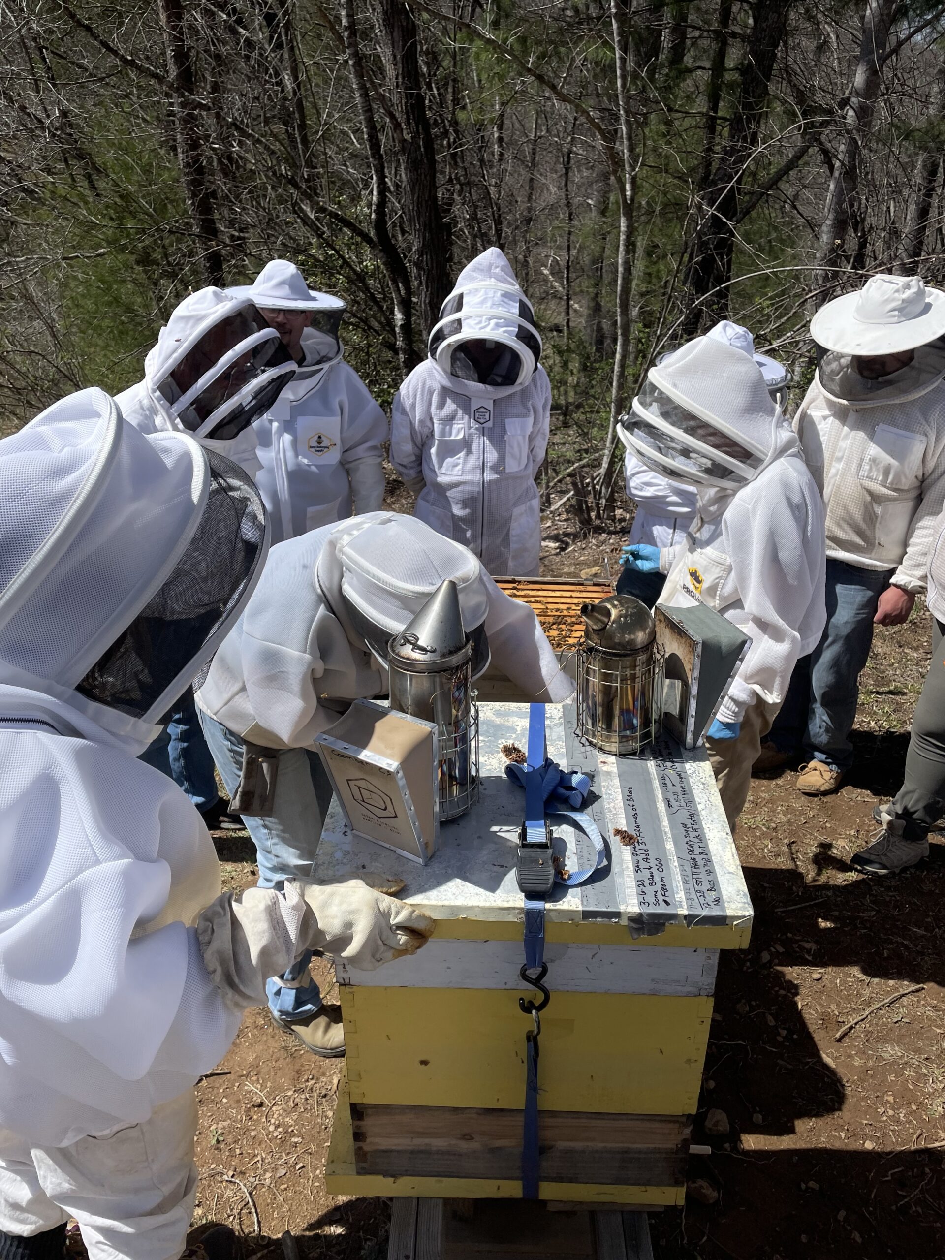 Students at the TCBA Bee Basics school gather around as an instructor shows them how to inspect a hive.